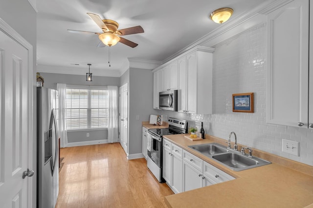 kitchen with light wood finished floors, a sink, white cabinets, appliances with stainless steel finishes, and crown molding