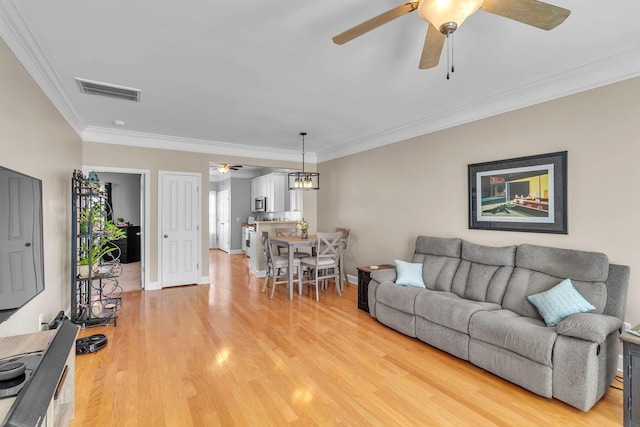 living room featuring visible vents, light wood-style floors, crown molding, baseboards, and ceiling fan