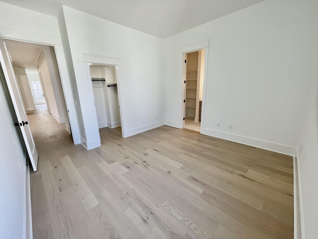 unfurnished bedroom with a closet, light wood-style flooring, a walk in closet, and baseboards