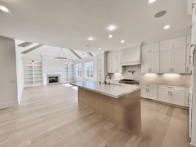 kitchen with custom exhaust hood, light wood-style flooring, a fireplace, a sink, and white cabinetry