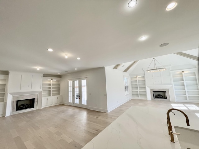 living room with light wood finished floors, a fireplace, french doors, and built in features