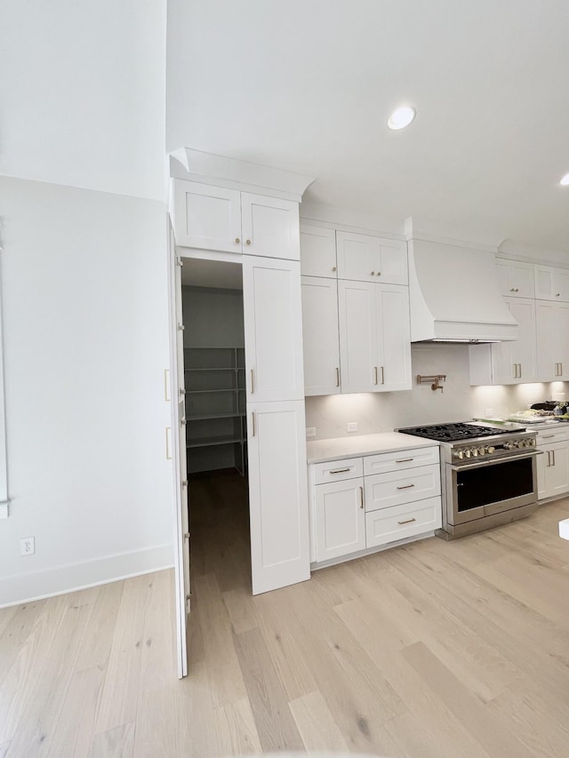 kitchen featuring custom exhaust hood, light wood-style flooring, stainless steel range, and white cabinetry