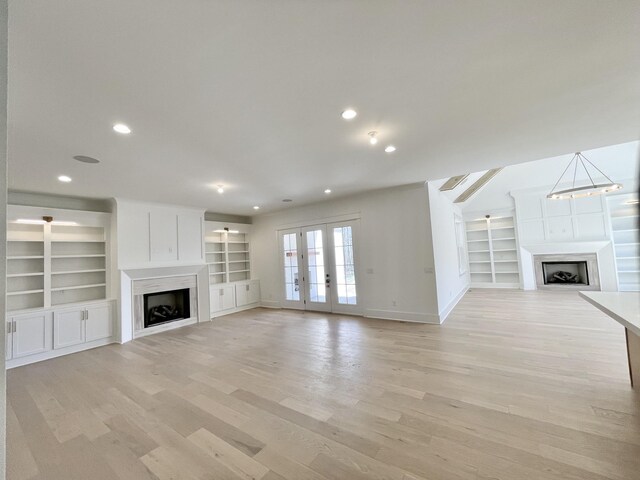 unfurnished living room with light wood-style flooring, a fireplace, baseboards, and french doors