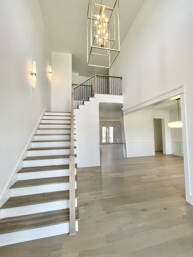 staircase featuring a high ceiling, wood finished floors, a wainscoted wall, and a chandelier