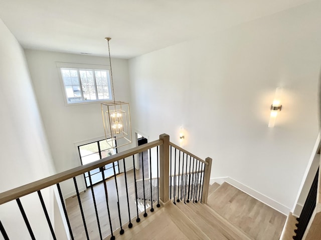 stairway featuring wood finished floors, baseboards, and a chandelier