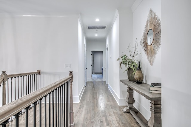 corridor with visible vents, crown molding, baseboards, an upstairs landing, and wood finished floors