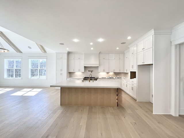 kitchen with light wood finished floors, a center island with sink, light countertops, white cabinets, and a sink