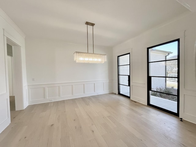 unfurnished dining area with light wood finished floors, a decorative wall, and a chandelier