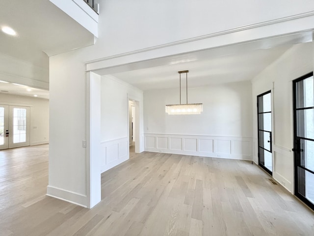 unfurnished dining area featuring light wood-type flooring, french doors, and a decorative wall