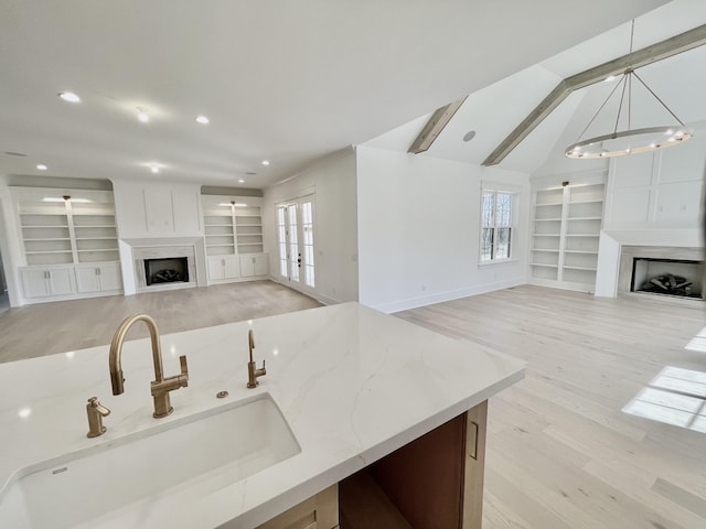 kitchen with built in shelves, a sink, light stone counters, open floor plan, and a fireplace