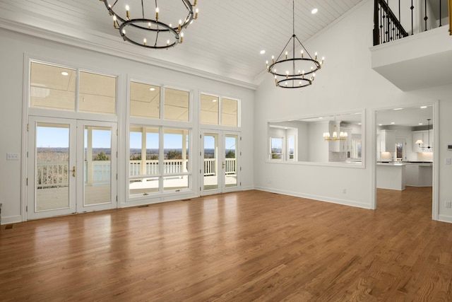 unfurnished living room with baseboards, a notable chandelier, wood finished floors, and high vaulted ceiling