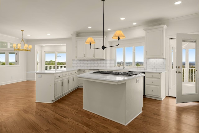 kitchen featuring a center island, light countertops, a peninsula, a notable chandelier, and white cabinetry