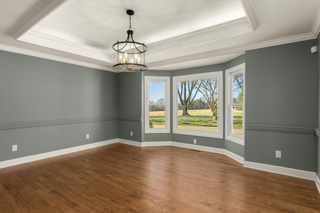 empty room with crown molding, a raised ceiling, and wood finished floors