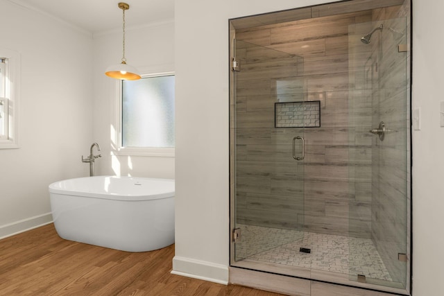 full bathroom with a shower stall, a freestanding tub, crown molding, and wood finished floors