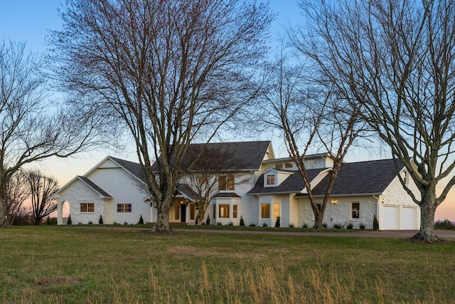 view of front of property featuring stone siding, an attached garage, and a front lawn