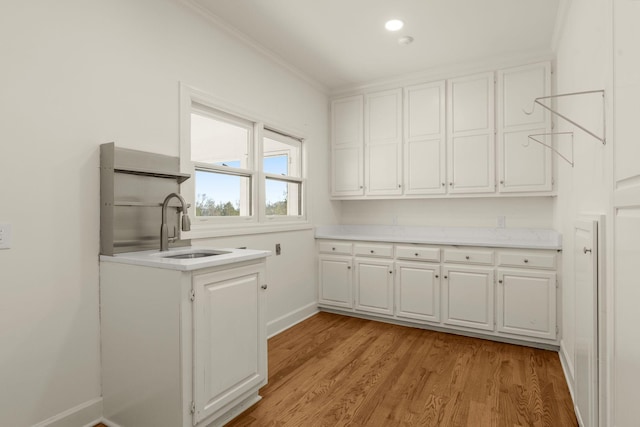 clothes washing area featuring light wood-style flooring, ornamental molding, baseboards, and a sink