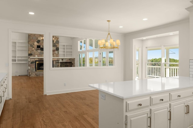 kitchen featuring a stone fireplace, white cabinets, wood finished floors, and ornamental molding