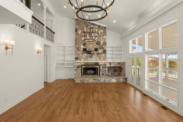 unfurnished living room featuring a stone fireplace, an inviting chandelier, built in shelves, and wood finished floors