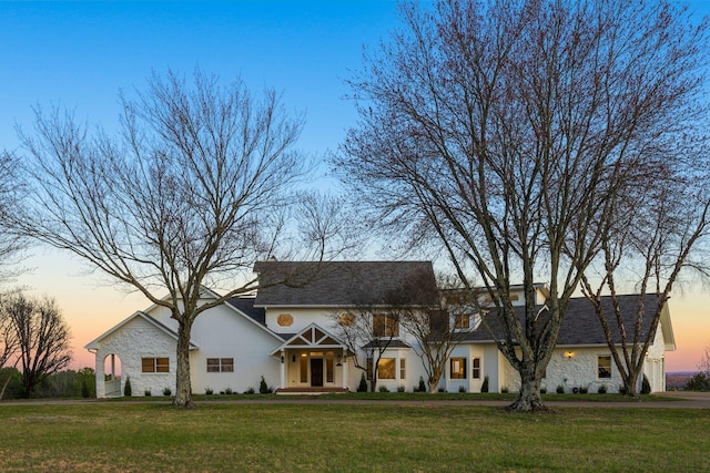 view of front of house with a front yard, stone siding, and stucco siding