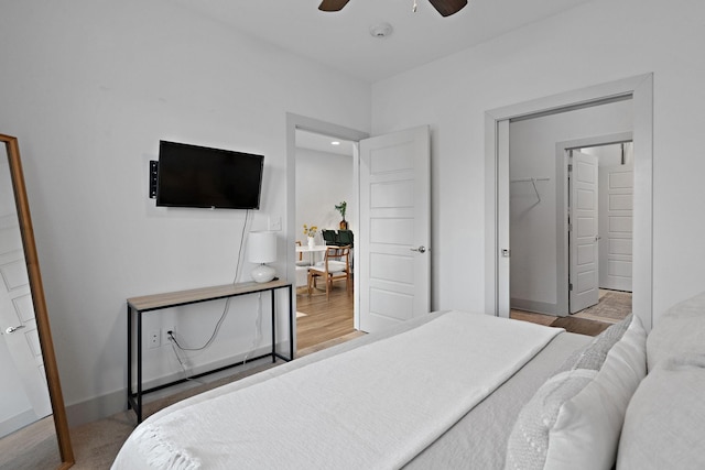 bedroom featuring baseboards, a spacious closet, wood finished floors, and a ceiling fan