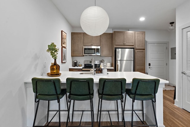 kitchen with a kitchen bar, wood finished floors, a peninsula, appliances with stainless steel finishes, and light countertops