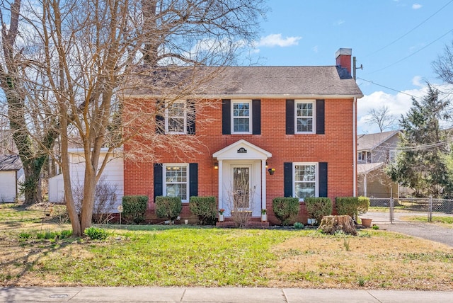 colonial inspired home featuring a gate, fence, a chimney, a front lawn, and brick siding