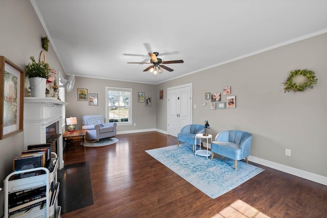 living area with baseboards, ornamental molding, a fireplace, wood finished floors, and a ceiling fan