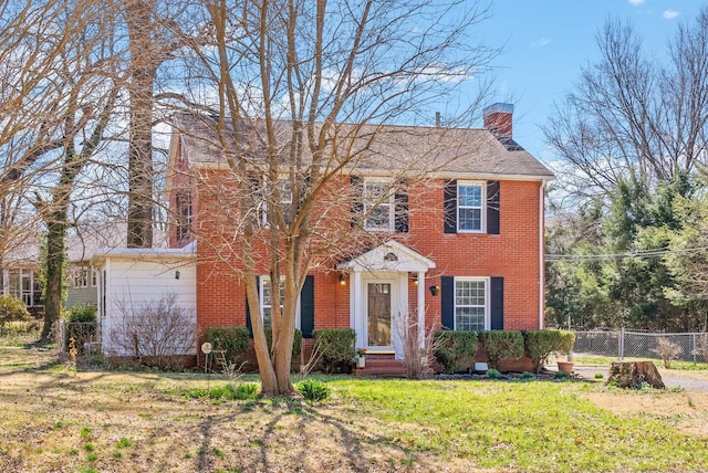 colonial-style house featuring brick siding, a front lawn, a chimney, and fence