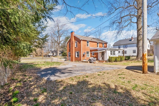 rear view of property with brick siding, fence, entry steps, a chimney, and driveway