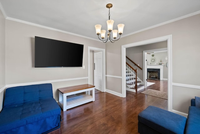 living area with wood finished floors, an inviting chandelier, a fireplace, stairs, and crown molding