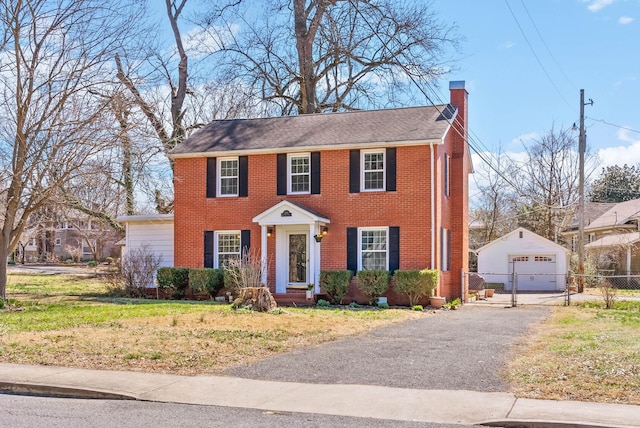 colonial home with an outbuilding, driveway, fence, brick siding, and a chimney