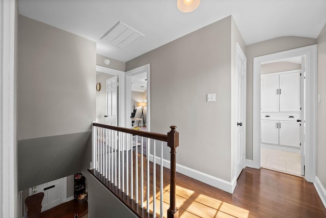 corridor with an upstairs landing, visible vents, baseboards, and wood finished floors