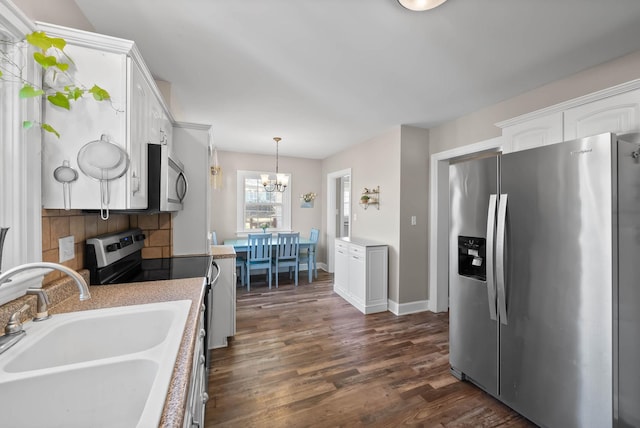 kitchen with stainless steel appliances, an inviting chandelier, dark wood-style floors, white cabinetry, and a sink