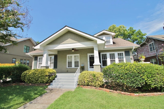 view of front of house featuring brick siding, a shingled roof, ceiling fan, a front yard, and covered porch