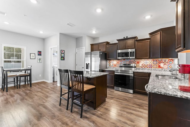 kitchen featuring a breakfast bar area, wood finished floors, dark brown cabinetry, appliances with stainless steel finishes, and tasteful backsplash