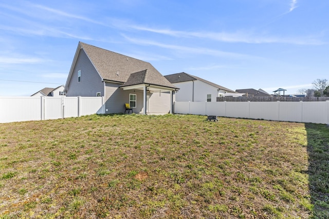 rear view of property featuring a yard, a fenced backyard, and a shingled roof