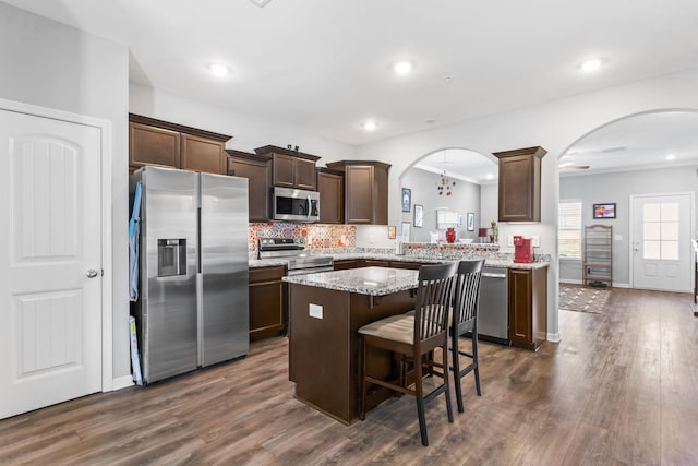 kitchen featuring dark brown cabinetry, arched walkways, appliances with stainless steel finishes, and a kitchen island