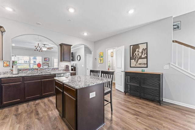 kitchen with dark brown cabinetry, a breakfast bar area, wood finished floors, arched walkways, and a sink