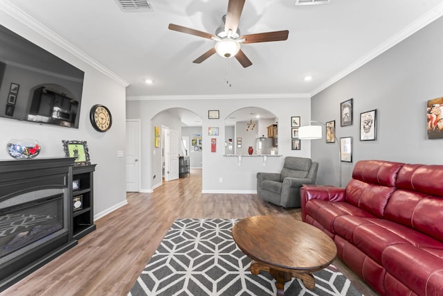 living area with visible vents, wood finished floors, arched walkways, crown molding, and baseboards