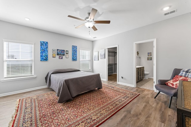 bedroom featuring visible vents, a ceiling fan, ensuite bathroom, wood finished floors, and baseboards