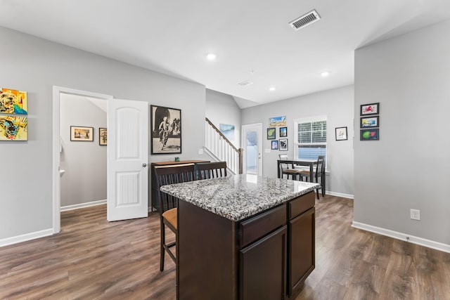 kitchen with visible vents, dark wood-style floors, a center island, a breakfast bar area, and dark brown cabinets