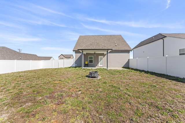 rear view of property with a yard, a fire pit, roof with shingles, and a fenced backyard