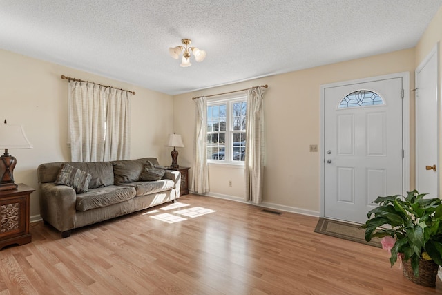 living area with visible vents, baseboards, a textured ceiling, and light wood finished floors