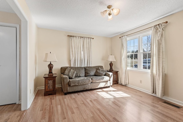 living area featuring visible vents, light wood-style floors, and a textured ceiling