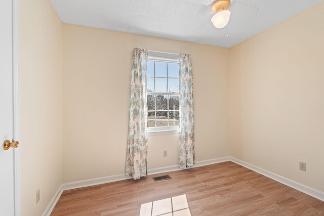 empty room featuring visible vents, a ceiling fan, a textured ceiling, light wood finished floors, and baseboards