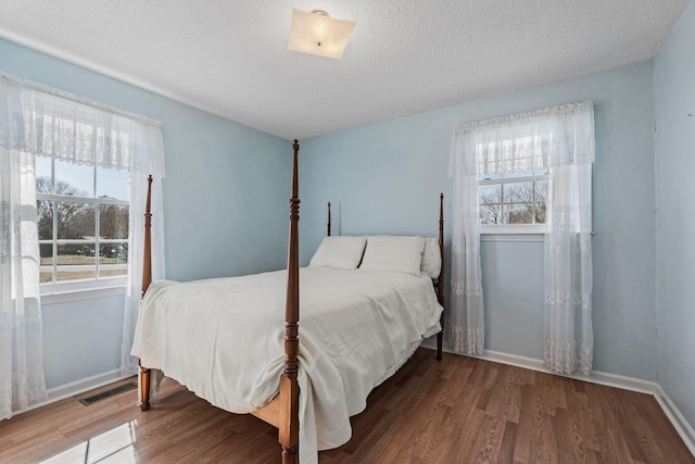 bedroom featuring visible vents, baseboards, a textured ceiling, and wood finished floors