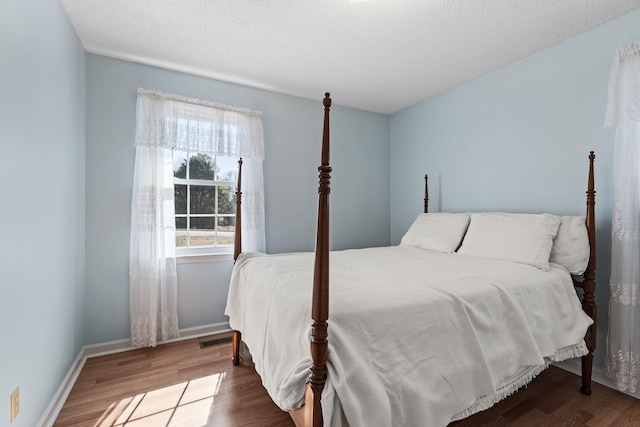 bedroom with visible vents, a textured ceiling, baseboards, and wood finished floors