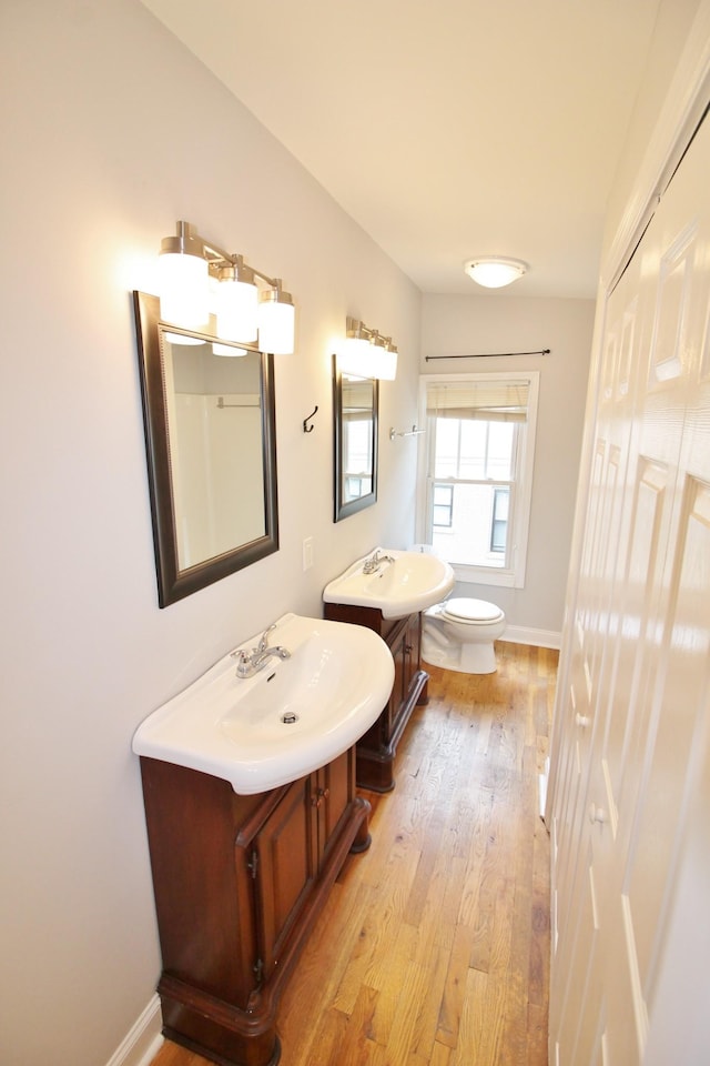 bathroom with toilet, wood-type flooring, baseboards, and a sink