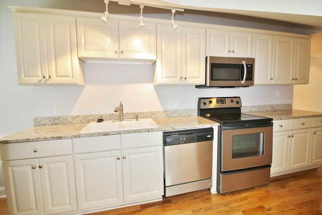 kitchen featuring light stone counters, light wood-style flooring, appliances with stainless steel finishes, white cabinets, and a sink