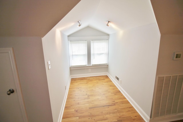 additional living space featuring visible vents, light wood finished floors, baseboards, and vaulted ceiling